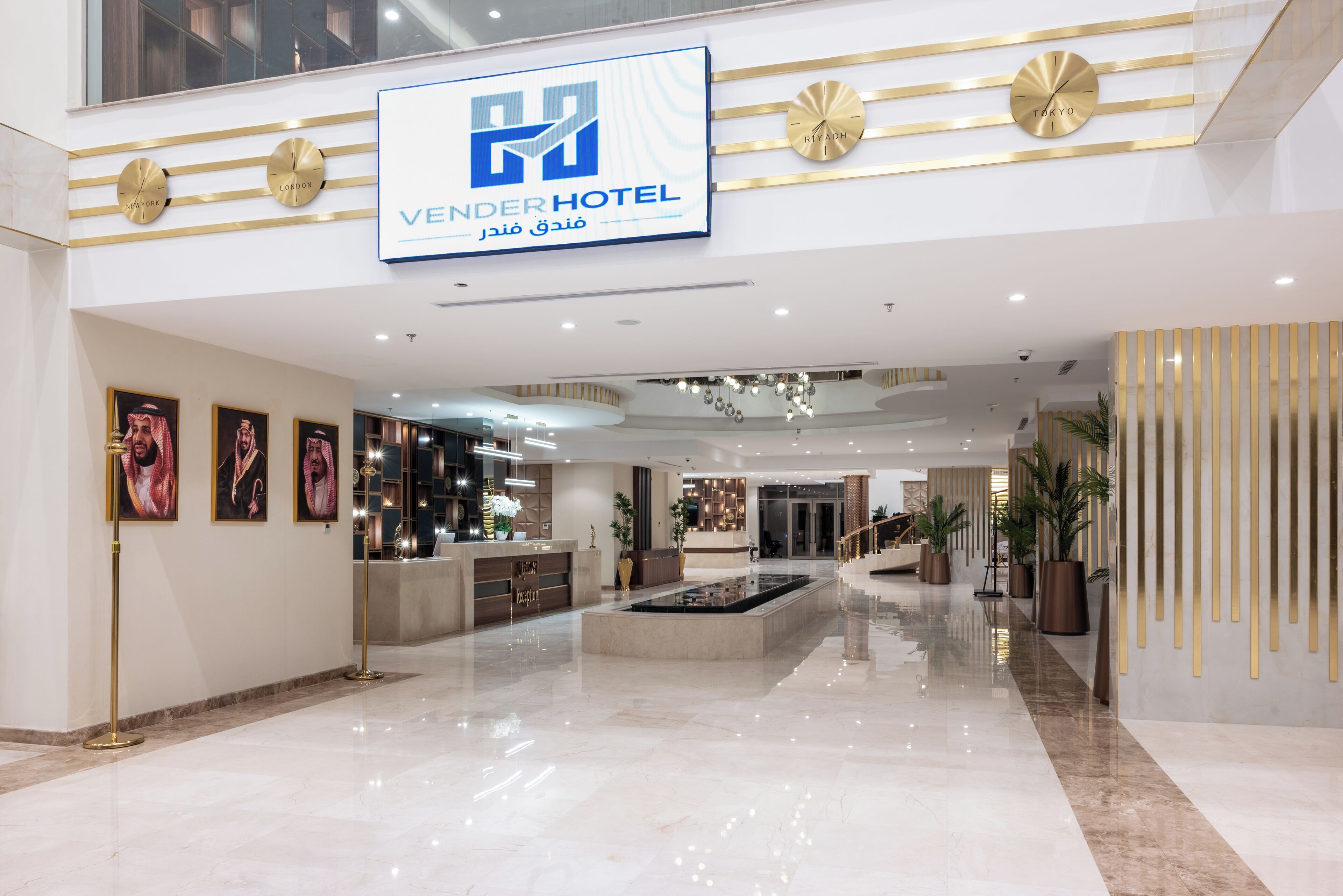 Un moderno vestíbulo de hotel con mostrador de recepción, obras de arte enmarcadas, fuente central y un cartel con el nombre del hotel.