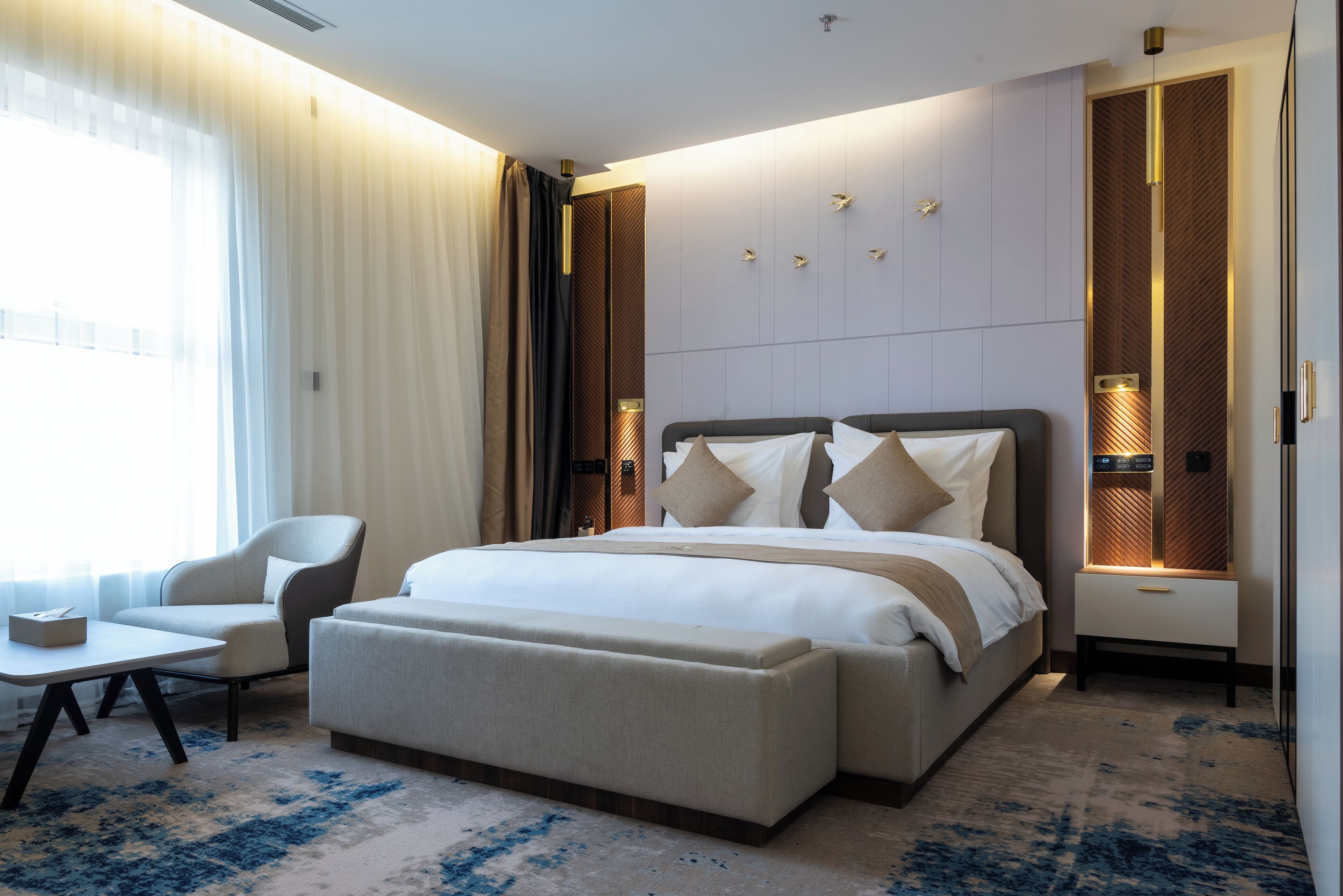 Een moderne hotelkamer met een groot bed, een zithoek met een tafel en uitzicht op de omgeving door grote ramen.