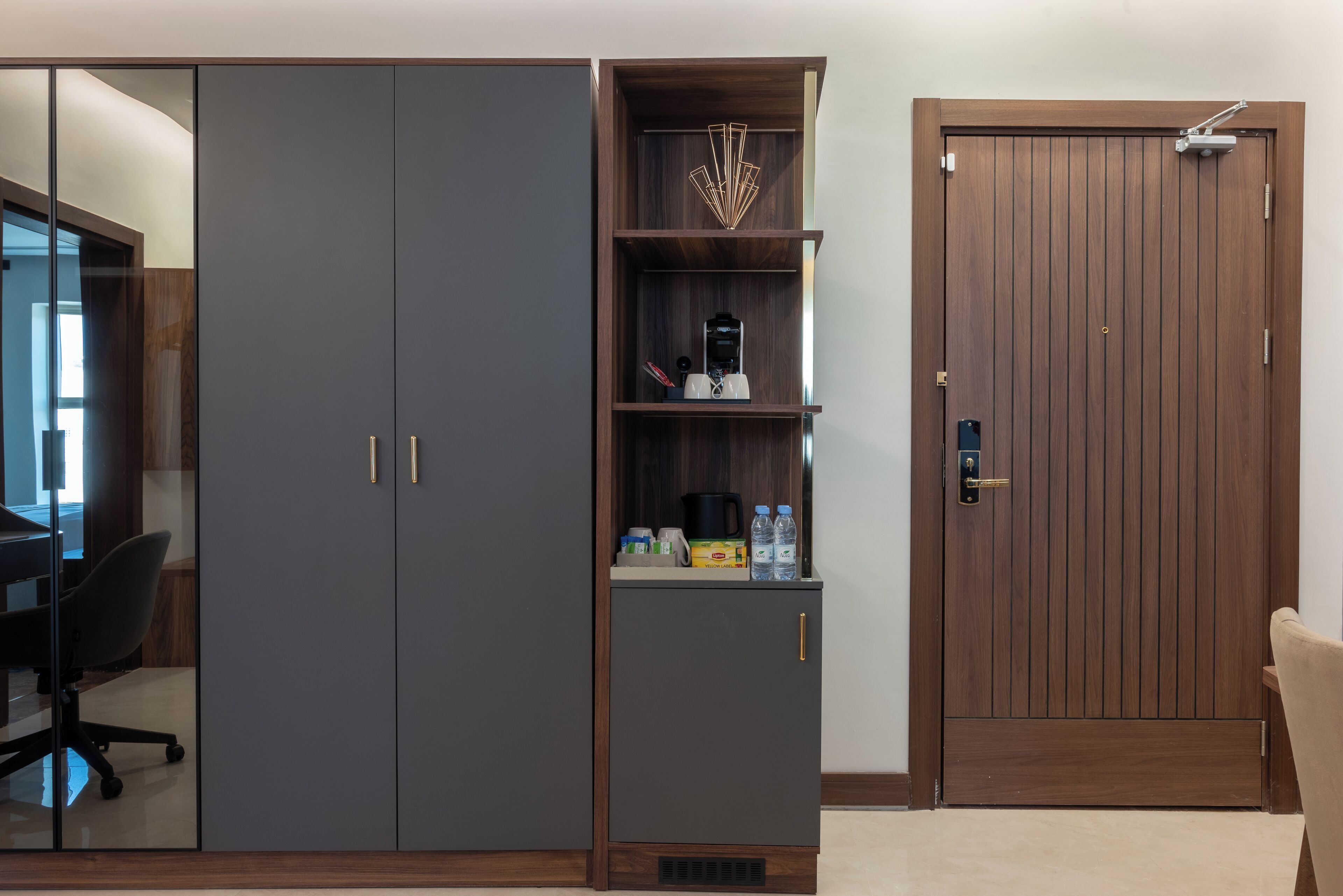 A room with a large wardrobe, a desk with a chair, and a wooden door.