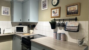 A kitchen with light blue cabinets, a microwave, a toaster, a stove, and a sink. There are wall-mounted shelves with kitchen utensils and a potted plant. - Llanidloes - Sleeps 7 - Parking - Pet Friendly (Llanidloes)