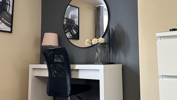 A modern office space with a white desk, a black mesh chair, a round mirror, a vase with flowers, and a clock on the wall. - Llanidloes - Sleeps 7 - Parking - Pet Friendly (Llanidloes)
