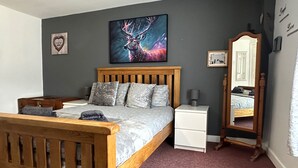A bedroom with a wooden bed, grey bedding, a nightstand, a bedside lamp, a mirror, and a wall art of a deer. - Llanidloes - Sleeps 7 - Parking - Pet Friendly (Llanidloes)