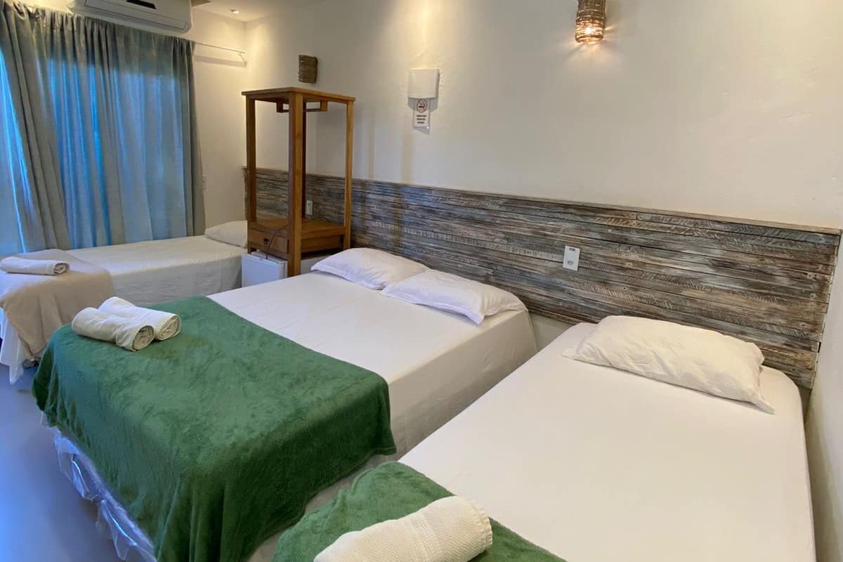 A hotel room with three single beds, a wooden headboard, a wall-mounted air conditioner, and a small table.