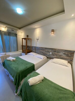 A hotel room with three single beds, a wooden headboard, a wall-mounted air conditioner, and a small table. - Pousada Preciosa (Búzios)