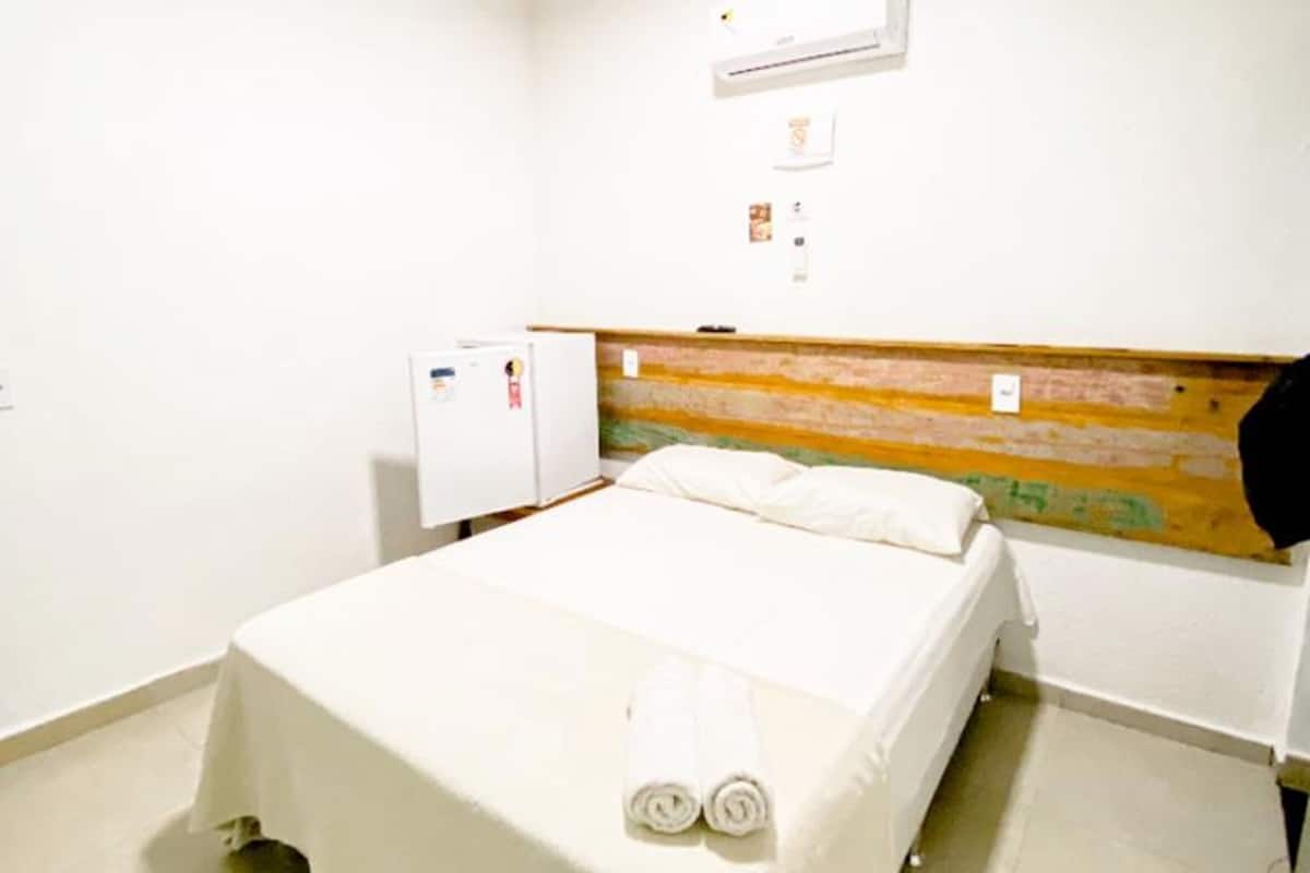 A hotel room with a bed, a small desk, an air conditioner, and a wall-mounted heater.