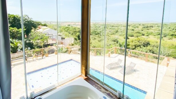 A large, white hot tub with a view of a swimming pool and lush greenery outside. - Pousada Preciosa (Búzios)