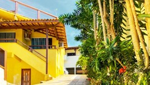 A yellow building with a staircase leading to a balcony, surrounded by greenery and red flowers. - Pousada Preciosa (Búzios)