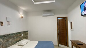 A hotel room with a bed, a TV, an air conditioning unit, and a wooden door. - Pousada Preciosa (Búzios)