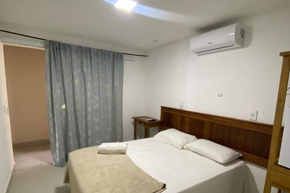 A neatly made bed with a wooden headboard, a bedside table, and an air conditioning unit on the wall.