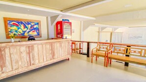 A reception area with a wooden reception desk, a Coca-Cola refrigerator, a colorful abstract painting, and a seating area with wooden benches. - Pousada Preciosa (Búzios)