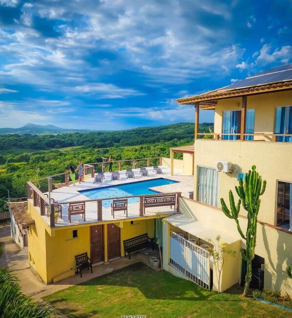 A pool with a view of mountains, a cactus, and a building with a yellow facade. - Pousada Preciosa (Búzios)