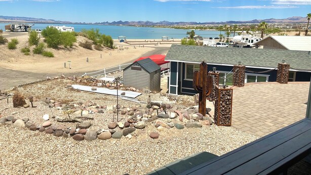 Blick auf ein Anwesen am Strand mit einer Terrasse, einem kleinen Schuppen und einem Gebäude mit rotem Dach.