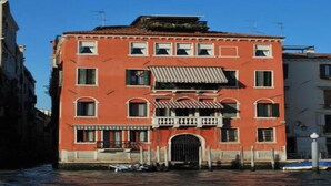A red building with a balcony and a black gate, located in a canal area.