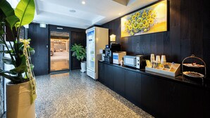 A reception area with a dark wood reception desk, a painting of sunflowers, a refrigerator, and a coffee machine. - shincheon noble stay hotel (Seoul)