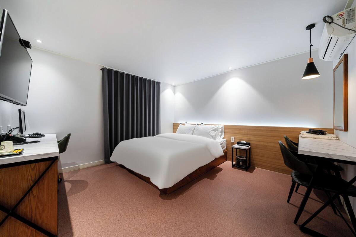 Habitación de hotel con cama, escritorio, silla, televisor y mesita de noche.