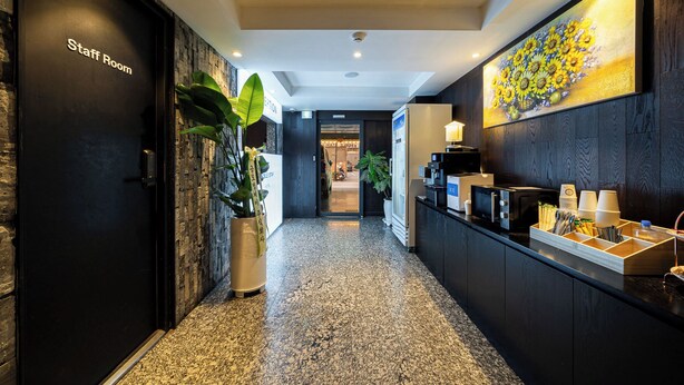A hotel reception area with a staff room, a reception desk, a potted plant, and a wall-mounted artwork. - shincheon noble stay hotel (Seoul)