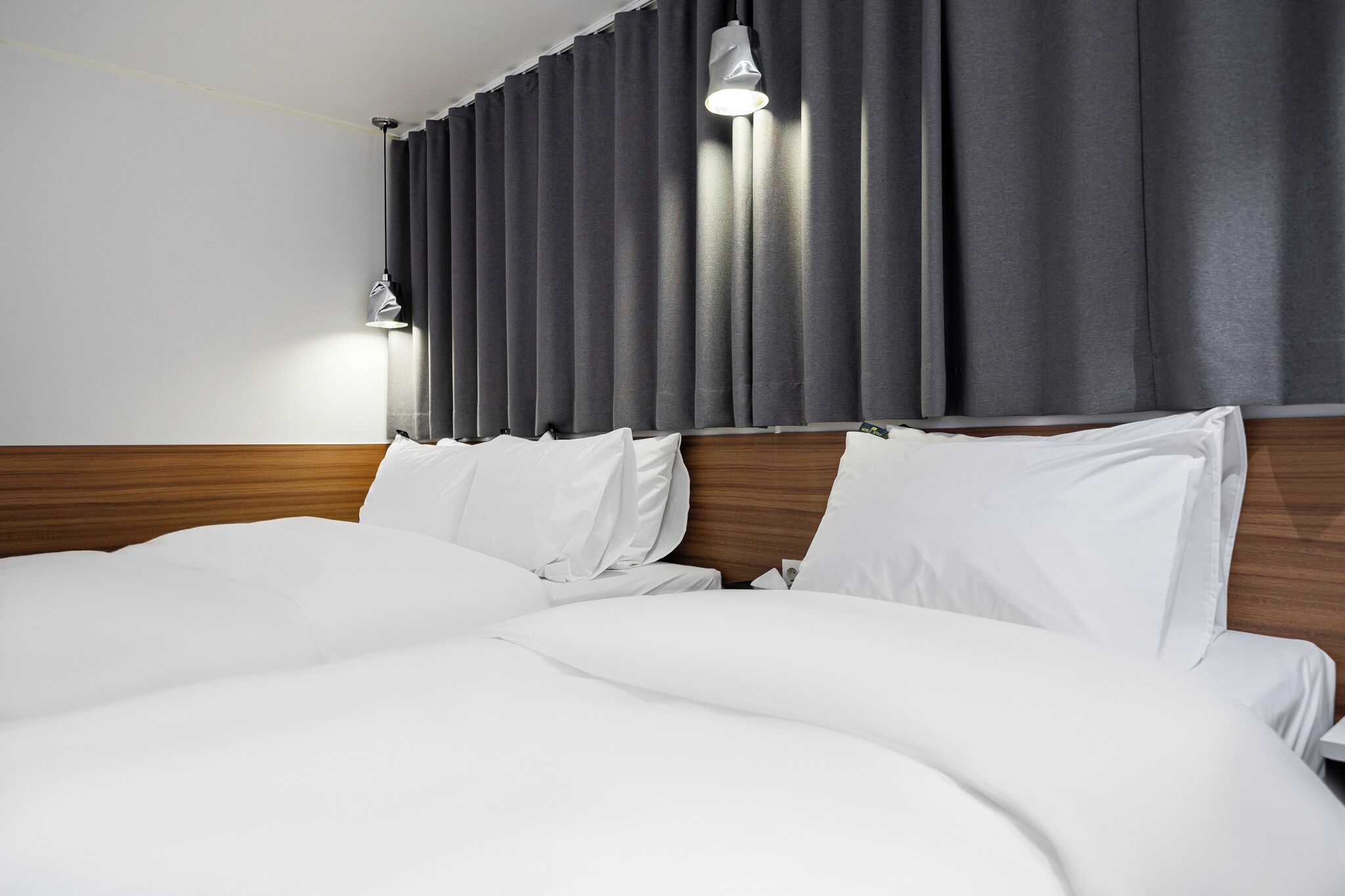 A hotel room with a large bed, wooden headboard, and a curtain-covered window.