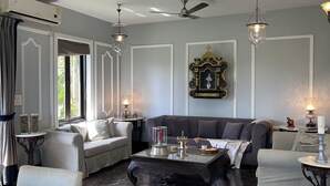 A living room with a grey sofa, a coffee table, and a chandelier. There is a window with curtains and an air conditioning unit on the wall. - Villa One - Pvt Pool Outdoor Deck North Goa (Nerul)