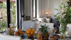 A dining area with a table set for two, featuring a fruit bowl, wine glasses, and a candle. - Villa One - Pvt Pool Outdoor Deck North Goa (Nerul)