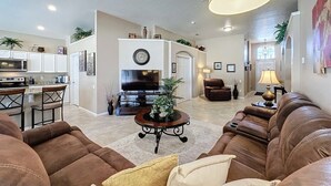 A spacious living room with a brown leather sofa, a coffee table, and a television. There is a kitchen area with a microwave and a dining table. - 4 Bed In Windsor Palms Resort - Steps To Disney 4 Bedroom Villa by RedAwning (Kissimmee)
