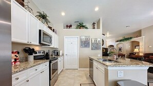 A modern kitchen with white cabinets, a microwave, and a sink. There is a small island with a trash can and a potted plant. - 4 Bed In Windsor Palms Resort - Steps To Disney 4 Bedroom Villa by RedAwning (Kissimmee)