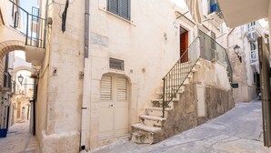 Ένας στενός δρόμος με μια σκάλα που οδηγεί σε ένα κτίριο με μπεζ πρόσοψη και μια πόρτα με παντζούρια.