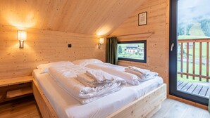 Ein Schlafzimmer einer Holzhütte mit zwei Betten, einem Fenster mit Blick auf ein Haus und einem Balkon.
