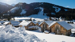 Un villaggio innevato con case in legno e una pista da sci sullo sfondo.