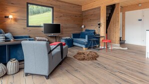 Un accogliente interno di una baita con arredamento in legno, una televisione, un divano, una poltrona e un tavolino.