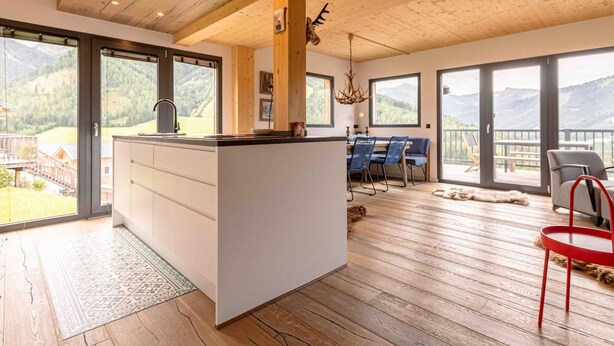 Un'ampia zona giorno con un'isola centrale, parquet e vista sulle montagne attraverso grandi finestre.
