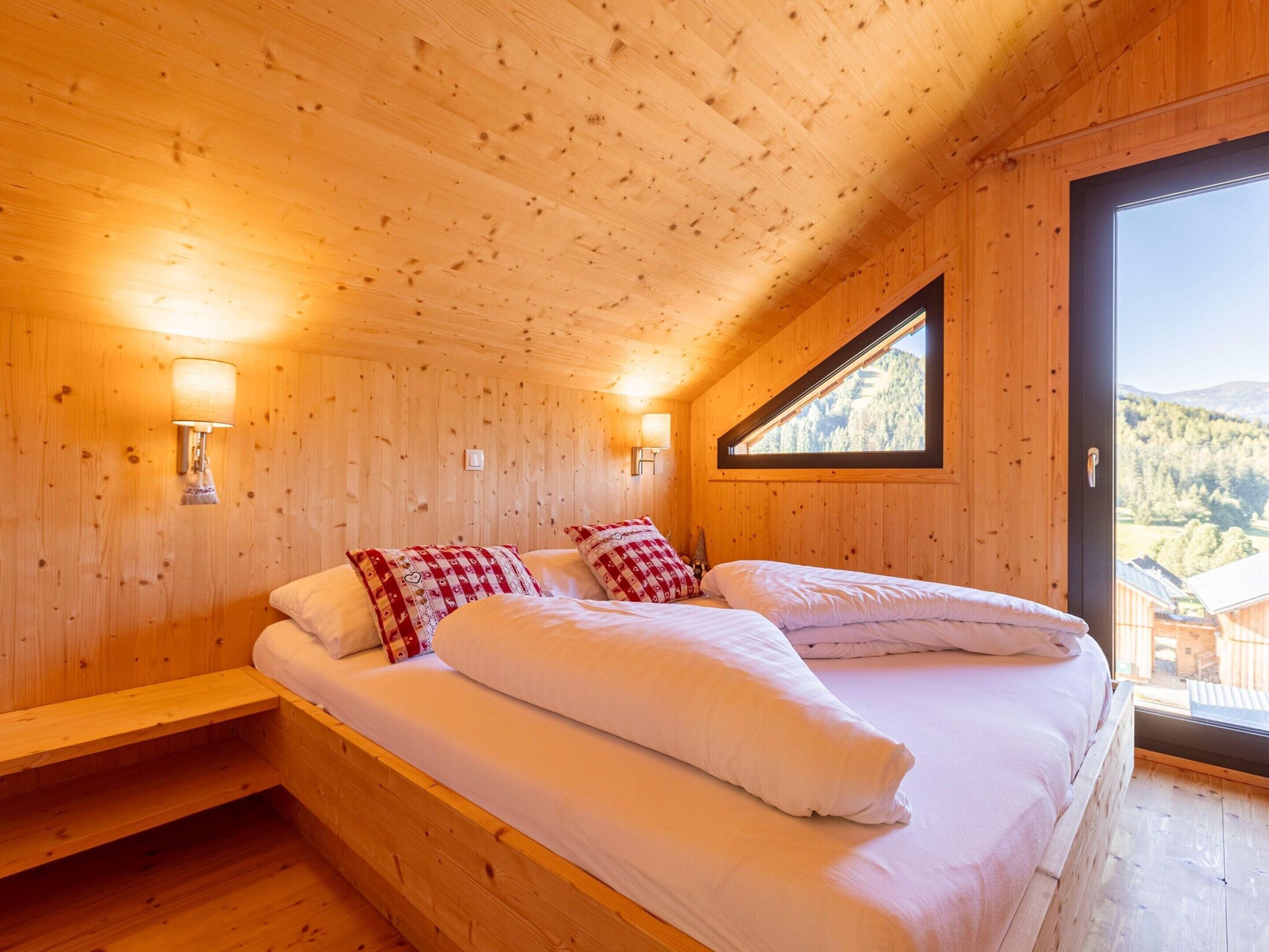 Ein Schlafzimmer einer Holzhütte mit zwei Betten, einem Fenster mit Bergblick und Wandlampen.