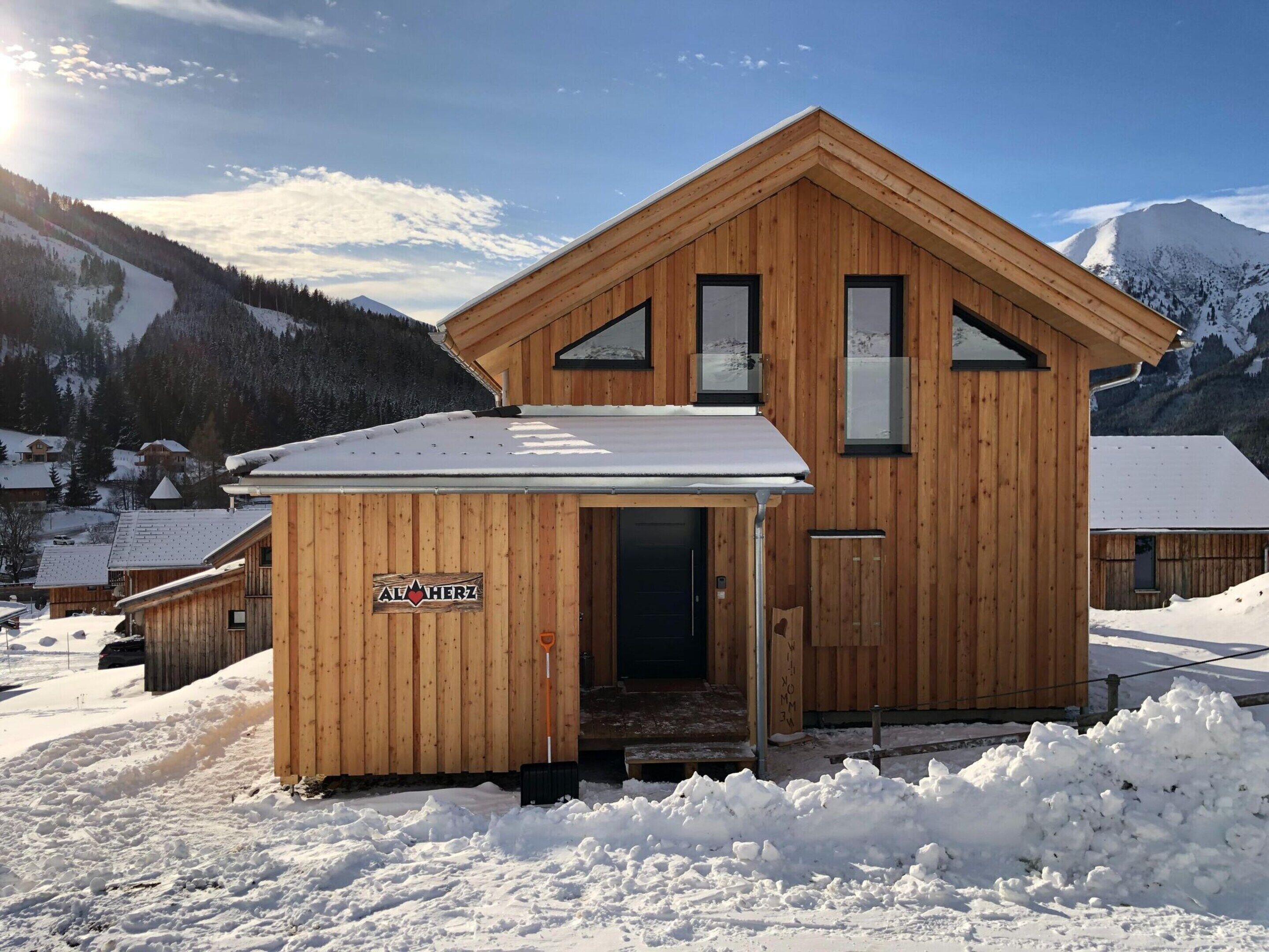 Una cabaña de madera con un letrero que dice "Alpaherz" en una zona montañosa nevada.