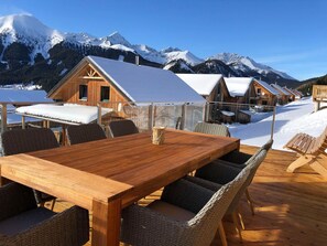 A wooden deck with a table and wicker chairs, overlooking snow-covered mountains. - Attractive Chalet With Infrared Sauna (Hohentauern)