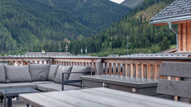 Une terrasse en bois avec un canapé et des tables, offrant une vue sur un paysage montagneux.