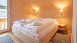 Une chambre dans une cabane en bois, avec un lit, deux lampes fixées au mur et une vue à travers une porte.