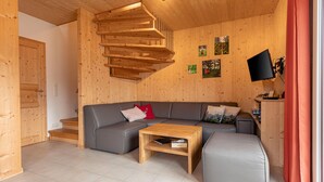 Un salon moderne avec un canapé d’angle gris, une table basse en bois et un téléviseur fixé au mur.