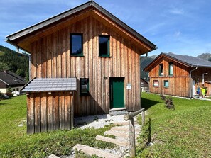Eine Holzhütte mit grüner Tür, einer kleinen Veranda und einem Kiesweg, der zum Eingang führt.