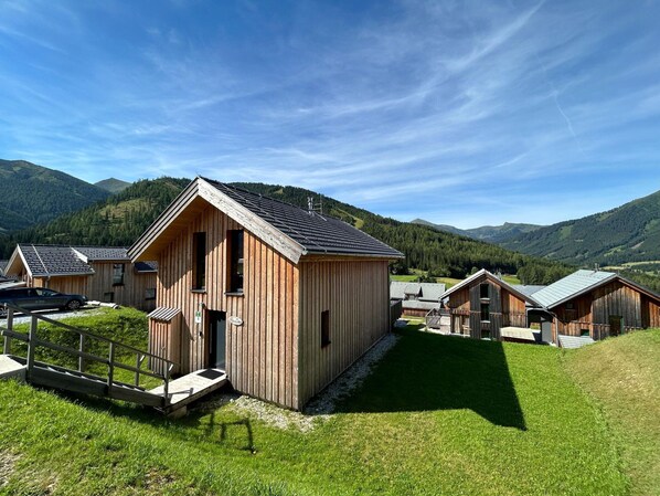 A wooden cabin with a sloped roof, surrounded by a well-maintained lawn and a mountain backdrop. - Cozy Chalet in Hohentauern: Your Alpine Retreat (Hohentauern)
