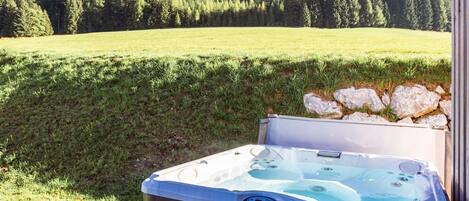 A hot tub on a wooden deck with a mountain and forest in the background.