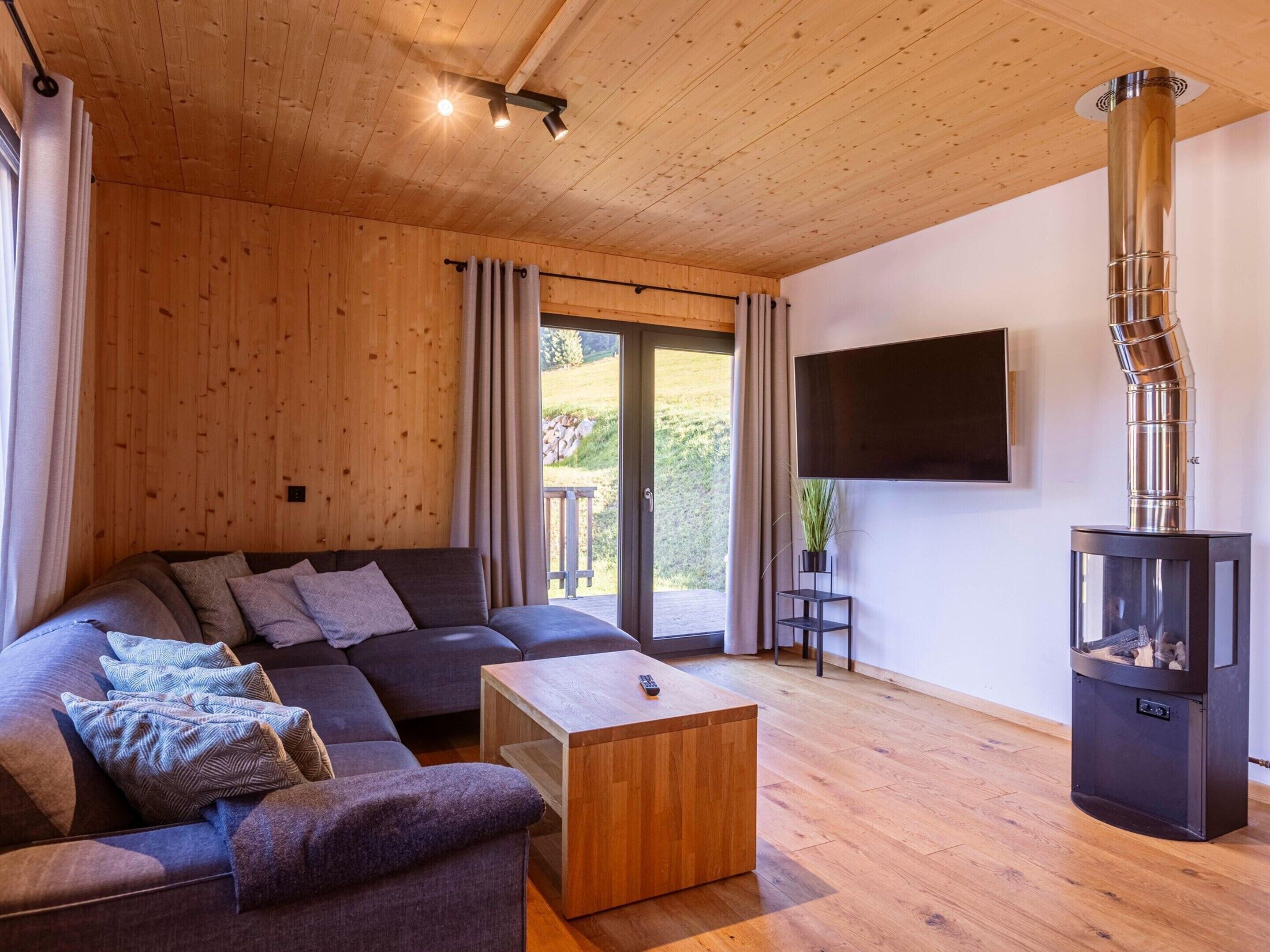 Una sala de estar moderna con techo de madera, un sofá modular, una mesa de centro, una chimenea y un televisor montado en la pared.