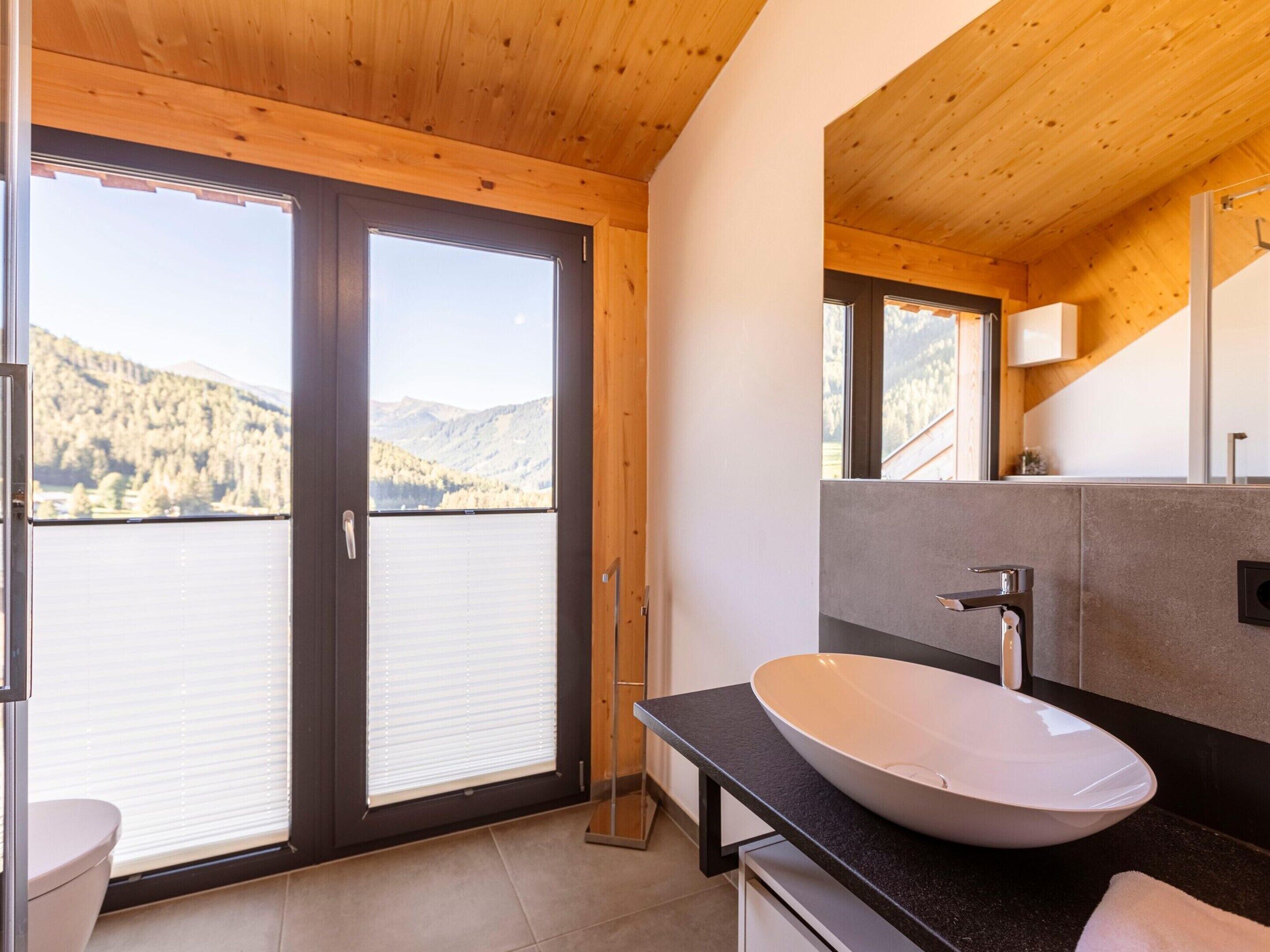 A modern bathroom with a large window, a white sink, and a mirror.