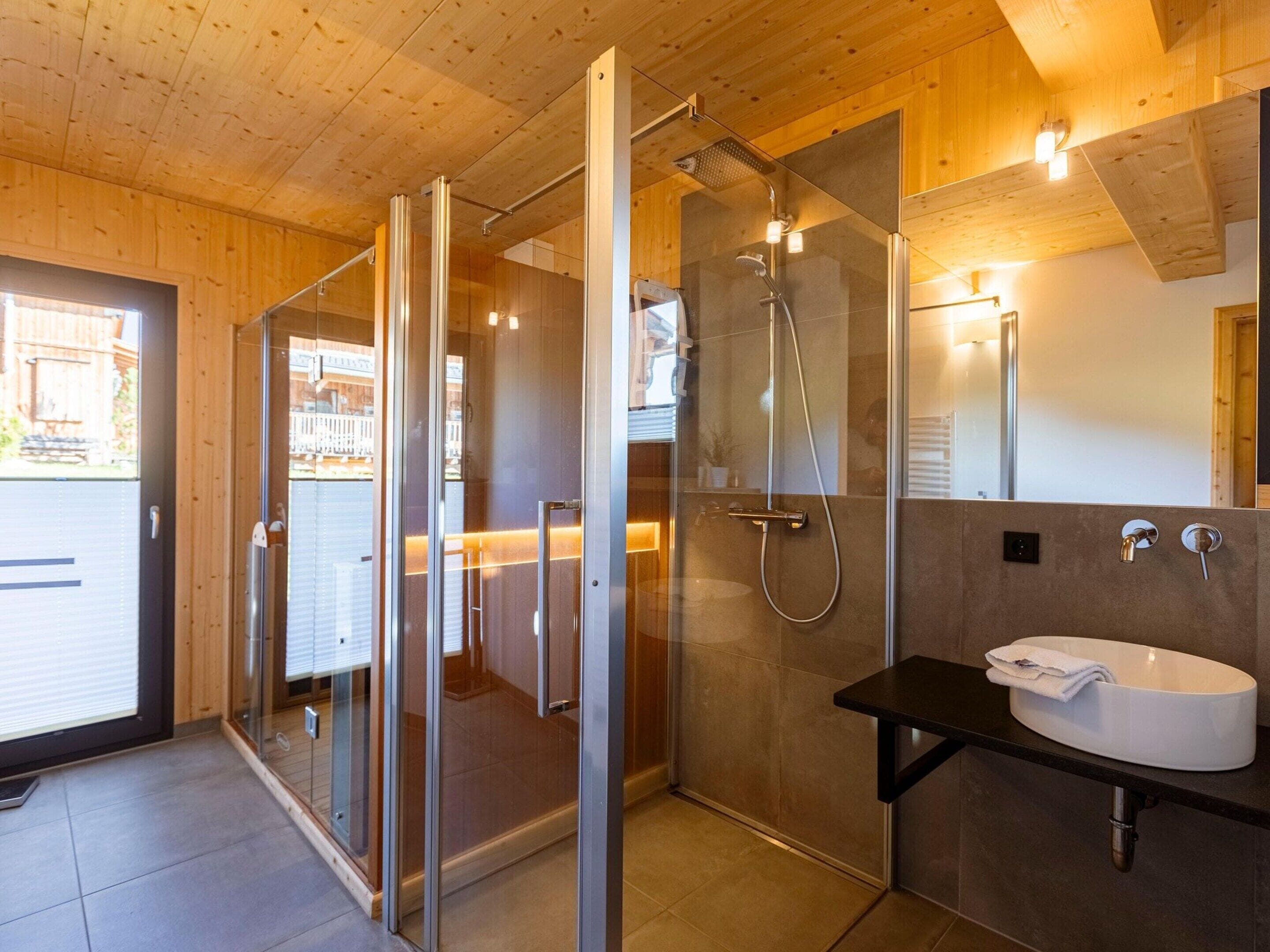 Un bagno moderno con cabina doccia in vetro, lavandino bianco e soffitto in legno.