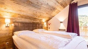 Ein Schlafzimmer mit Holzboden, zwei Betten, einem Nachttisch und einem Fenster mit Vorhängen.