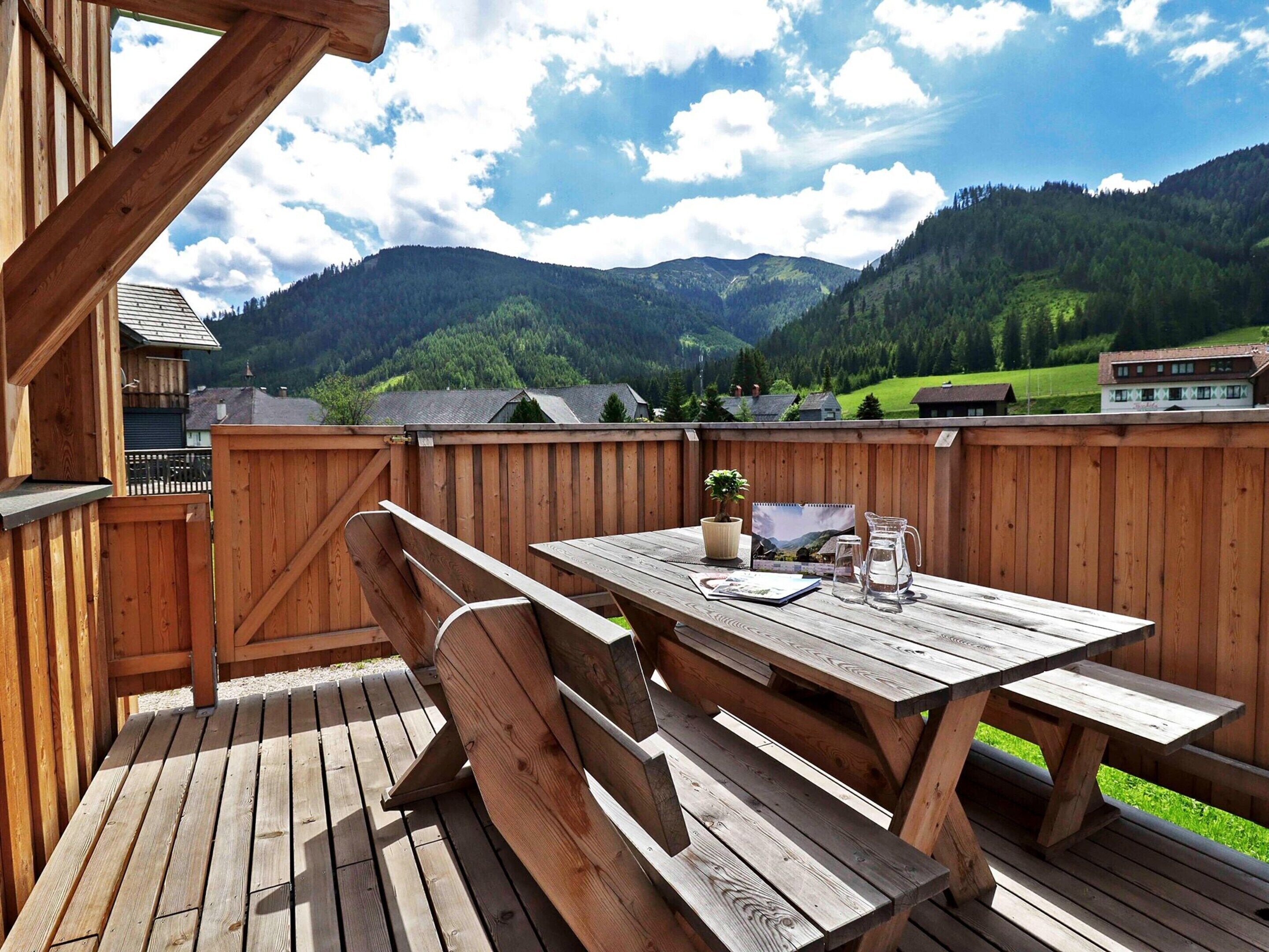 A wooden deck with a picnic table and benches, overlooking a mountainous landscape.