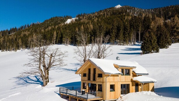 Une cabane en bois dotée d’un balcon, entourée d’un paysage enneigé et d’arbres.