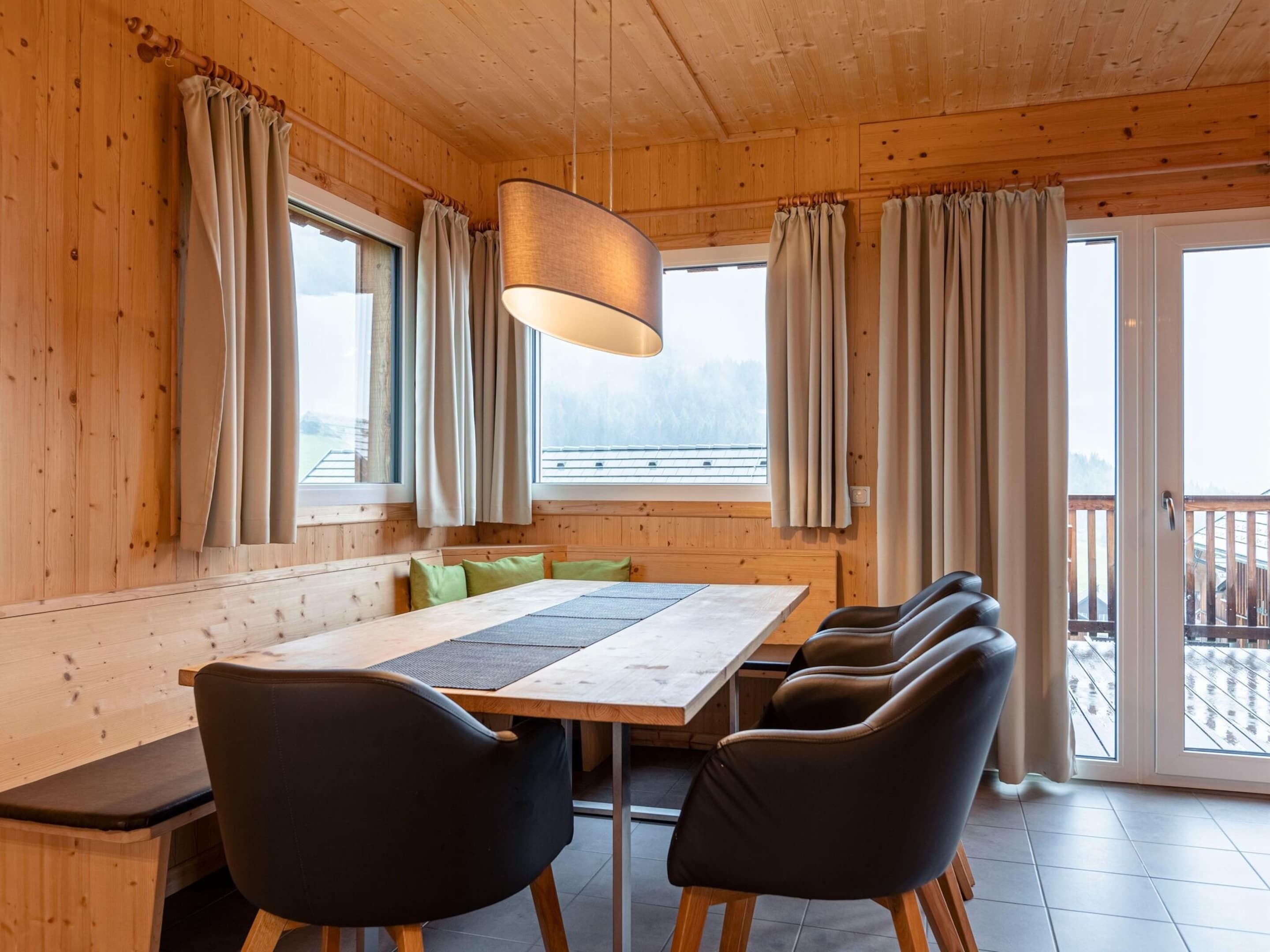 Interior de una cabaña de madera con una mesa de comedor, sillas y cortinas.