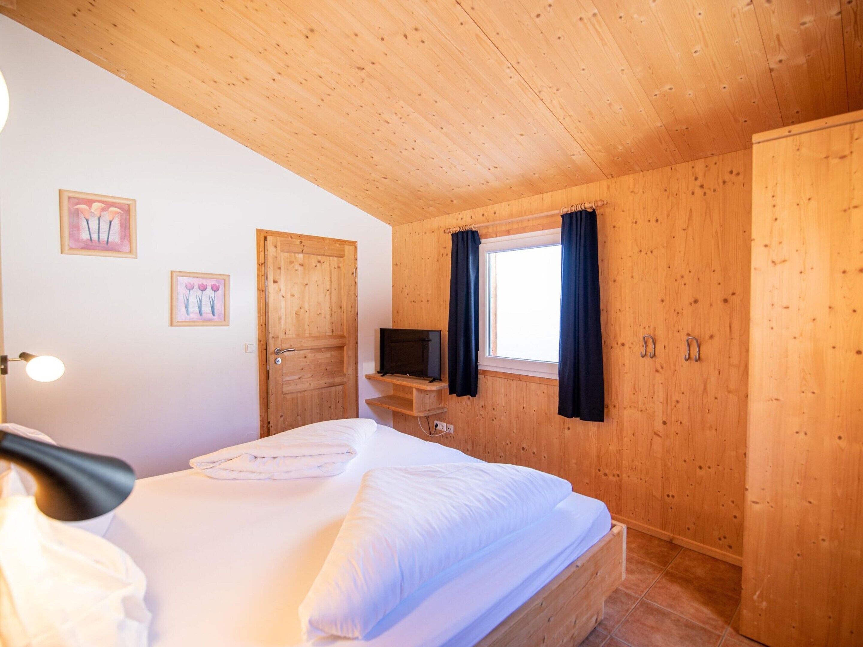 Une pièce aux murs lambrissés, avec un lit, un téléviseur posé sur un meuble et deux portes.