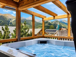A hot tub with a wooden deck and a view of mountains and a flag. - Chalet in Hohentauern With an Outdoor hot tub (Hohentauern)