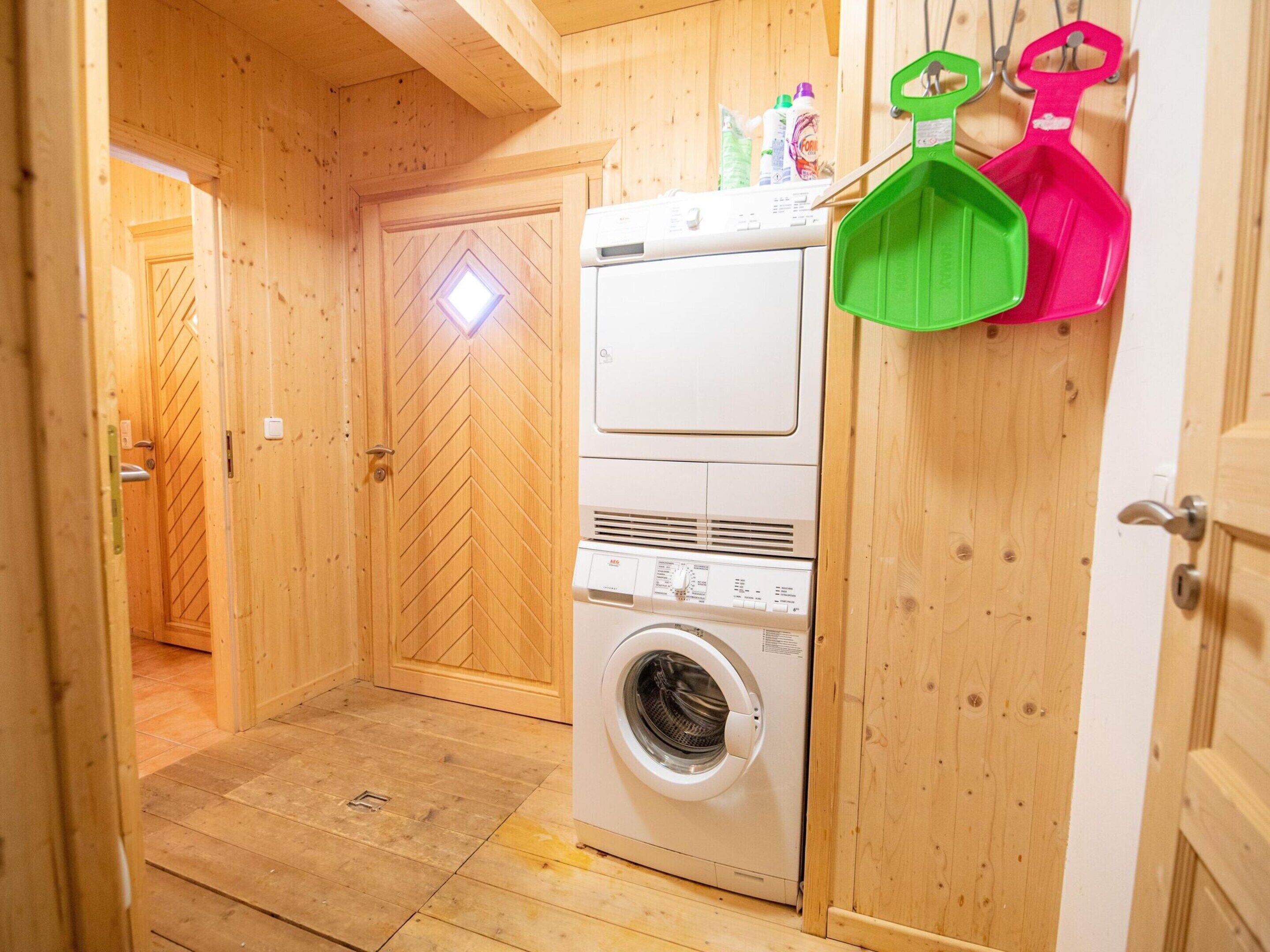 A laundry room with a washing machine and dryer, wooden walls, and a door with a diamond-shaped window.