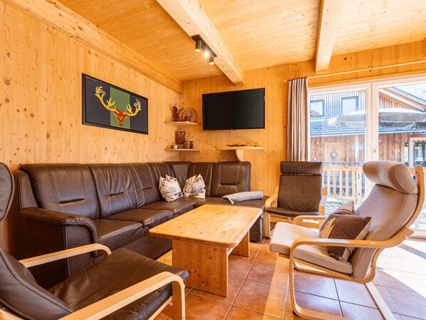 A wooden cabin interior with a sofa, chairs, a table, a TV, and a balcony with a view. - Chalet in Hohentauern Near Ski Slopes (Hohentauern)